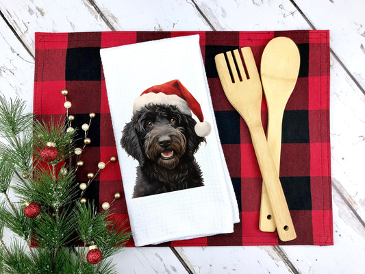 A black goldendoodle wearing a santa hat on a kitchen tea towel as a gift