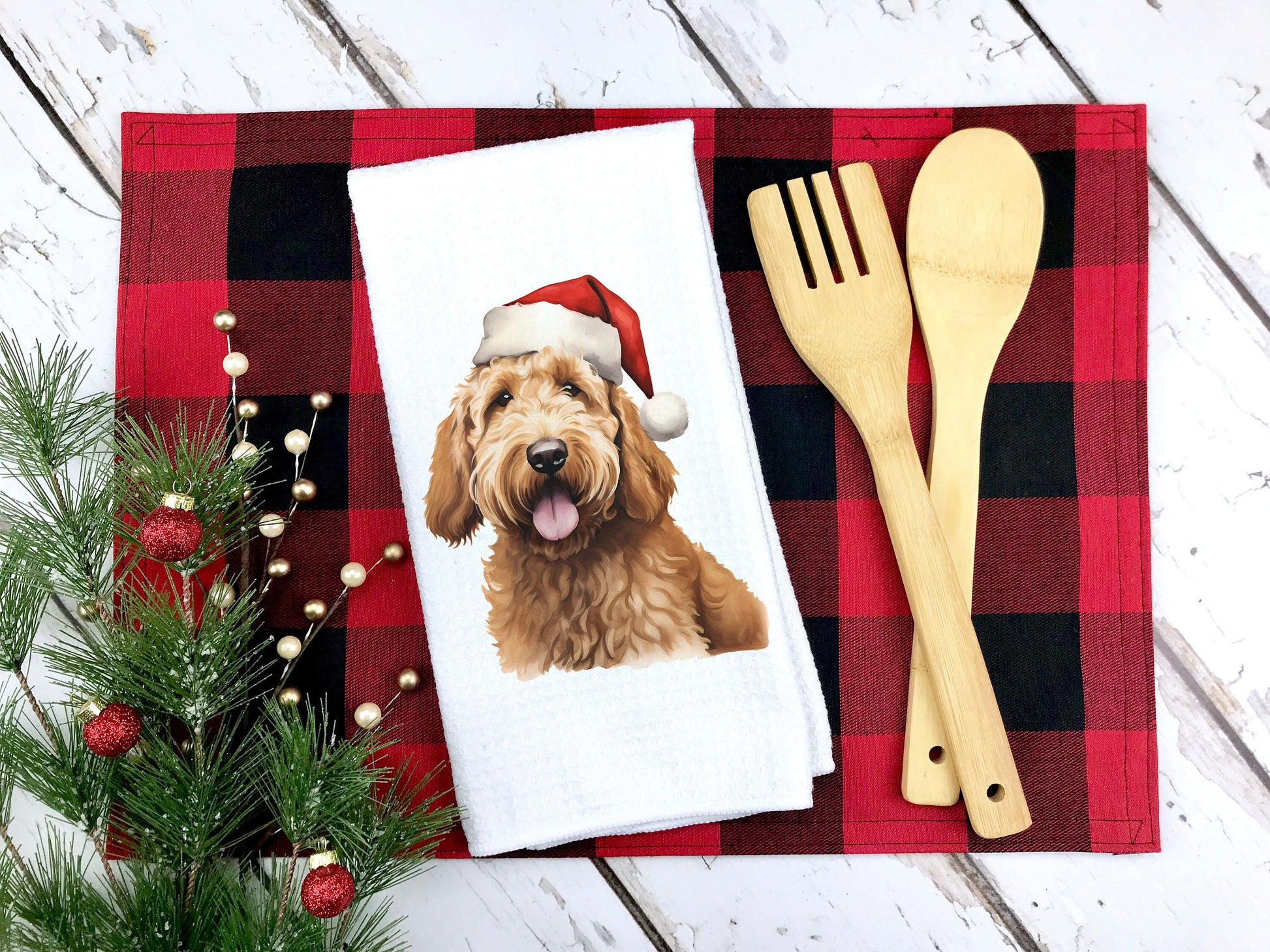 A yellow goldendoodle dog wearing a santa hat on a tea towel as a Christmas gift