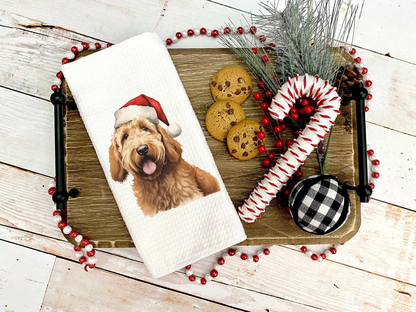 A yellow goldendoodle dog wearing a santa hat on a tea towel as a Christmas gift