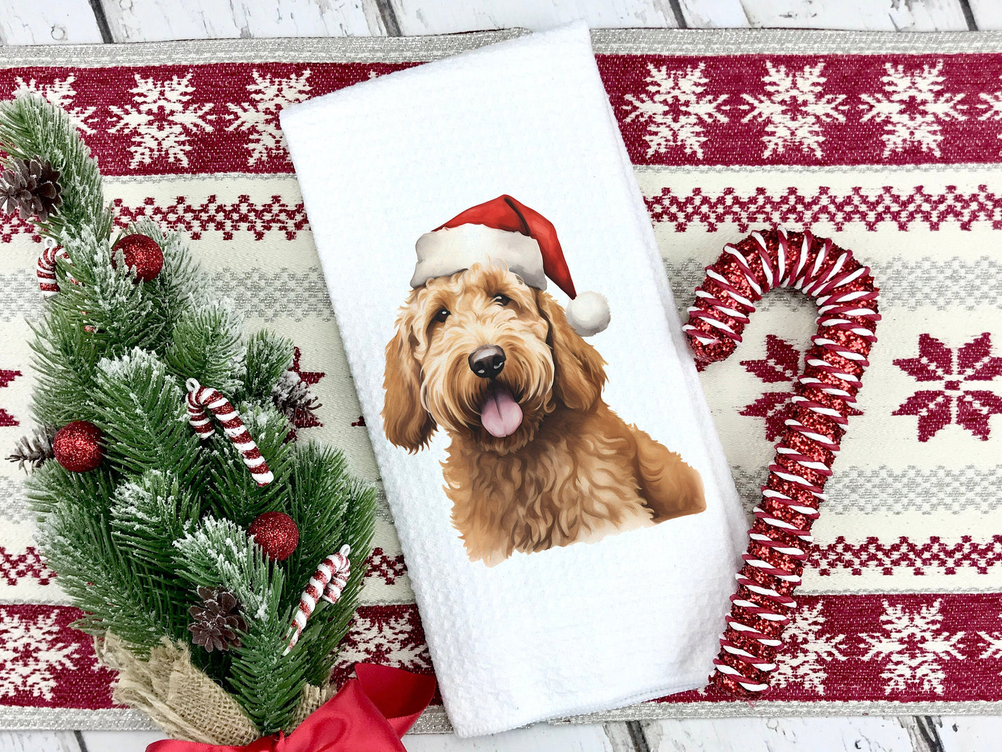 A yellow goldendoodle dog wearing a santa hat on a tea towel as a Christmas gift